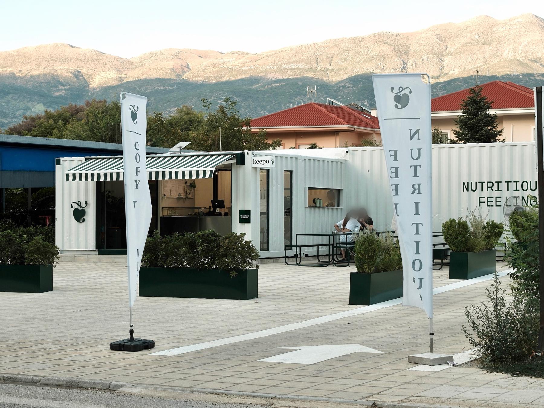 Το Keepo από έξω — λευκά containers με πράσινη τέντα, με τα βουνά των Ιωαννίνων στο βάθος